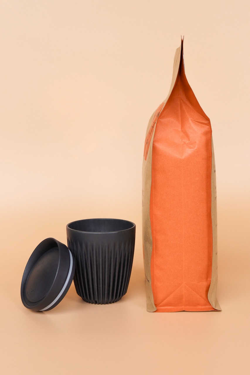 A bag of 1kg Organic Coffee next to a Black Huskee Keep Cup