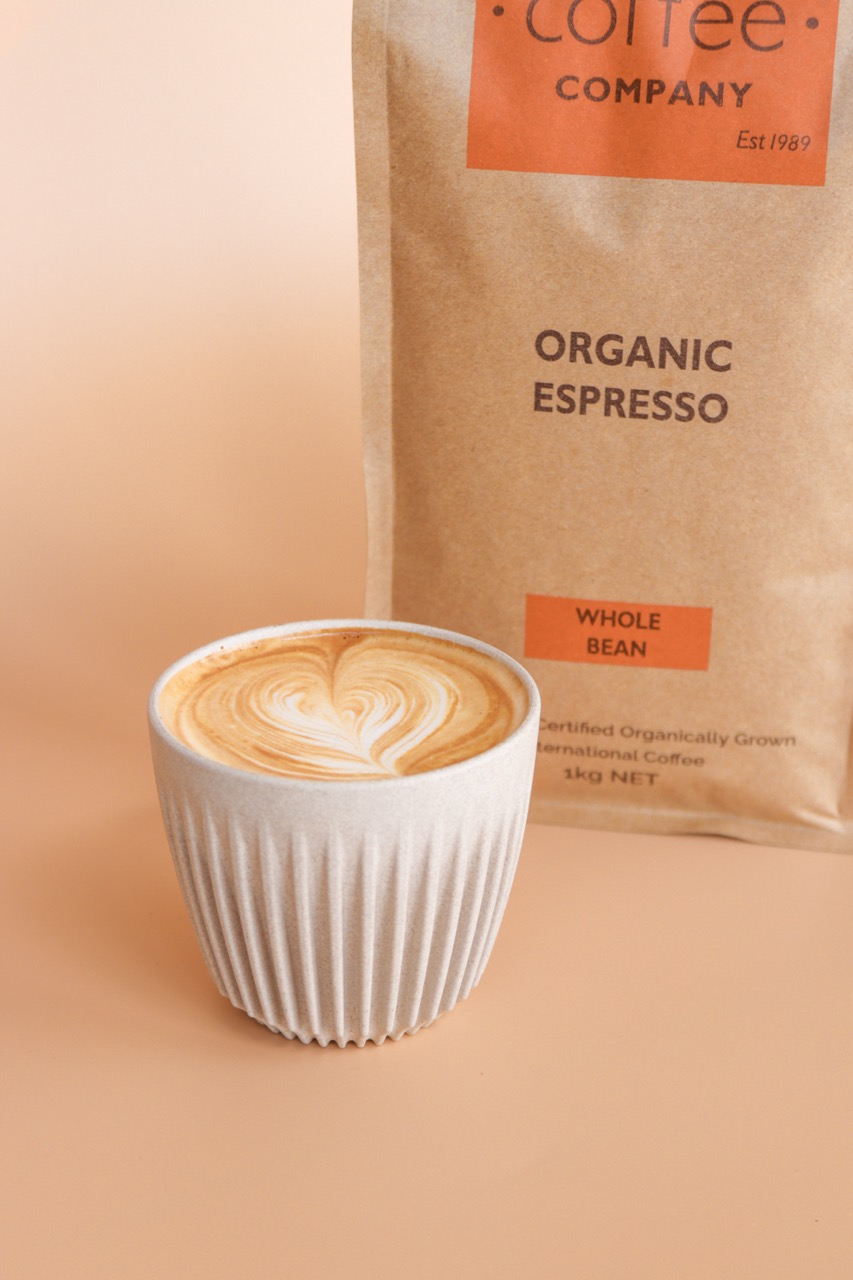 A bag of 1kg Organic Coffee next to a latte coffee served in a White Huskee Keep Cup