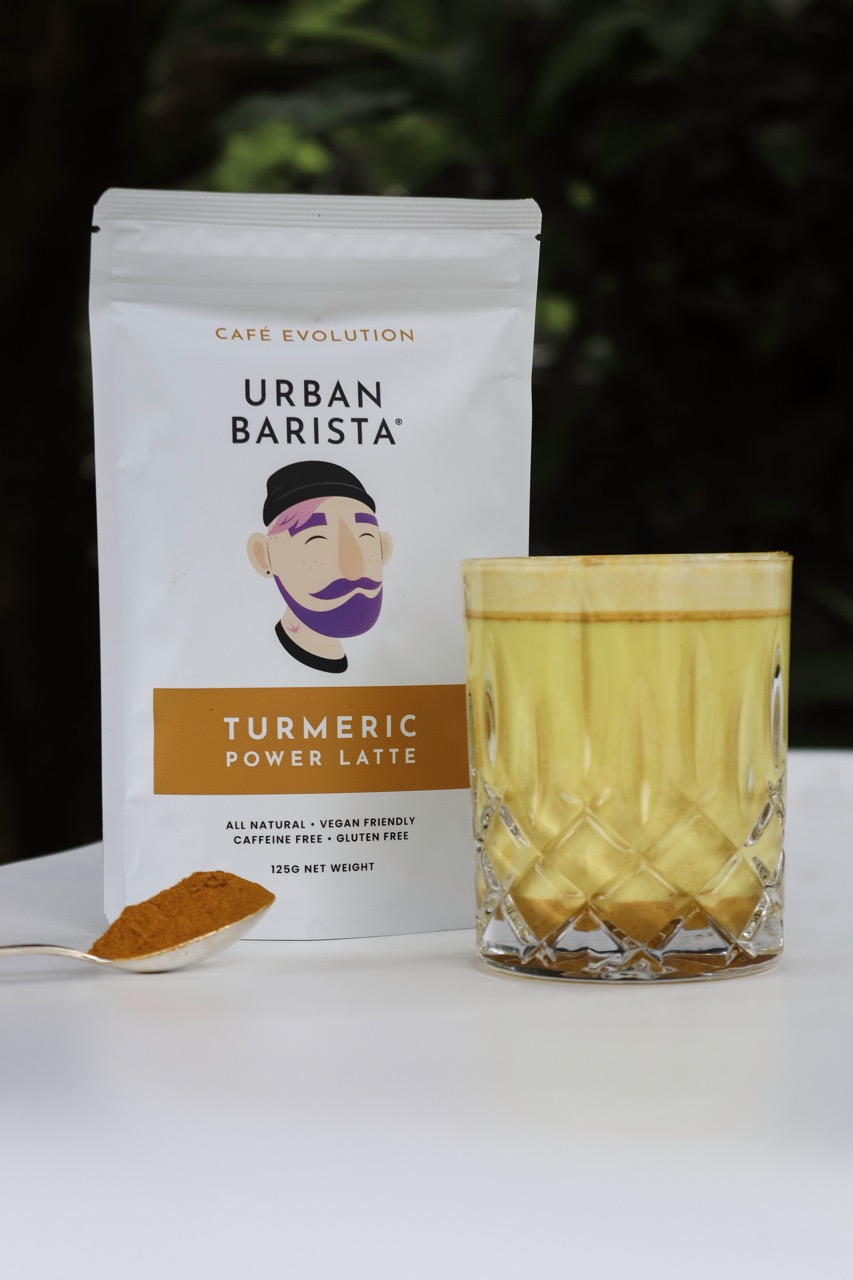 Turmeric latte in a glass next to a pouch of Urban Barista turmeric power latte mix